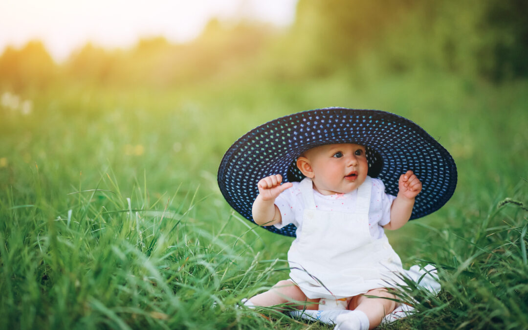 bébé assis dans l'herbe portant un chapeau trop grand pour elle